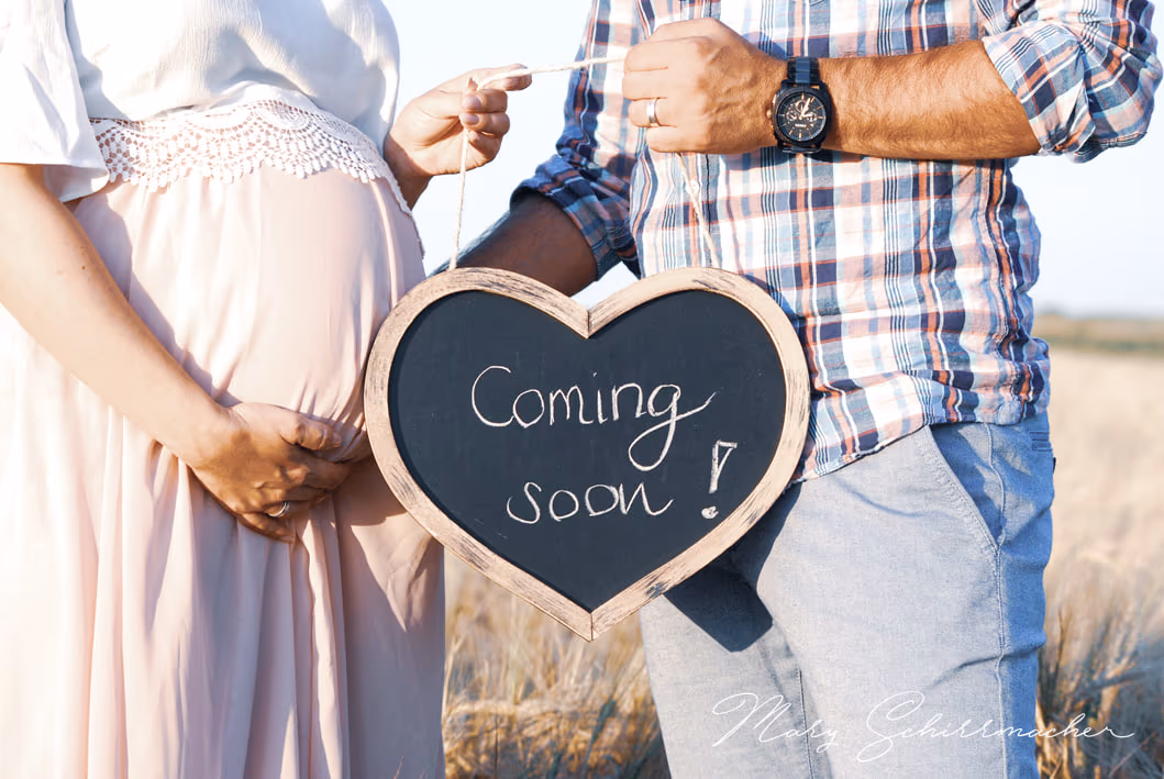 Zwei Hände halten ein herzförmiges Schild vor einen Babybauch