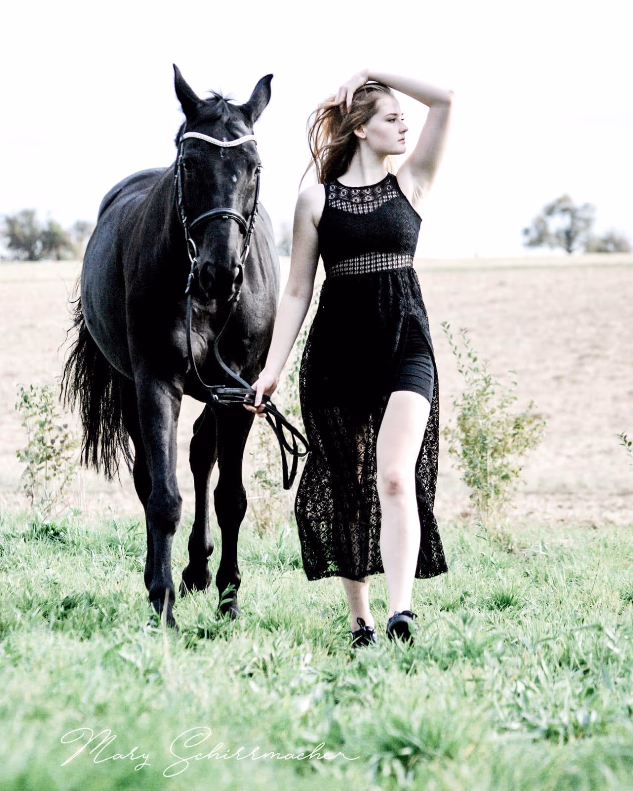 Frau im schwarzen Kleid neben einem schwarzen Pferd auf einem Feld