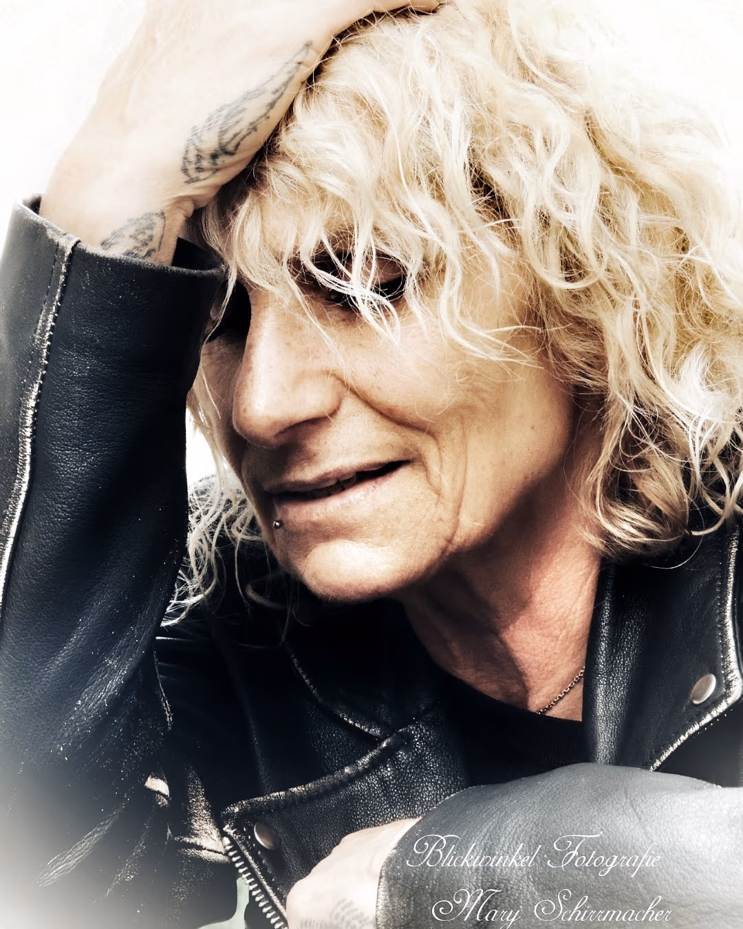 Frau mit blonden Locken in Lederjacke, die Hand im Haar
