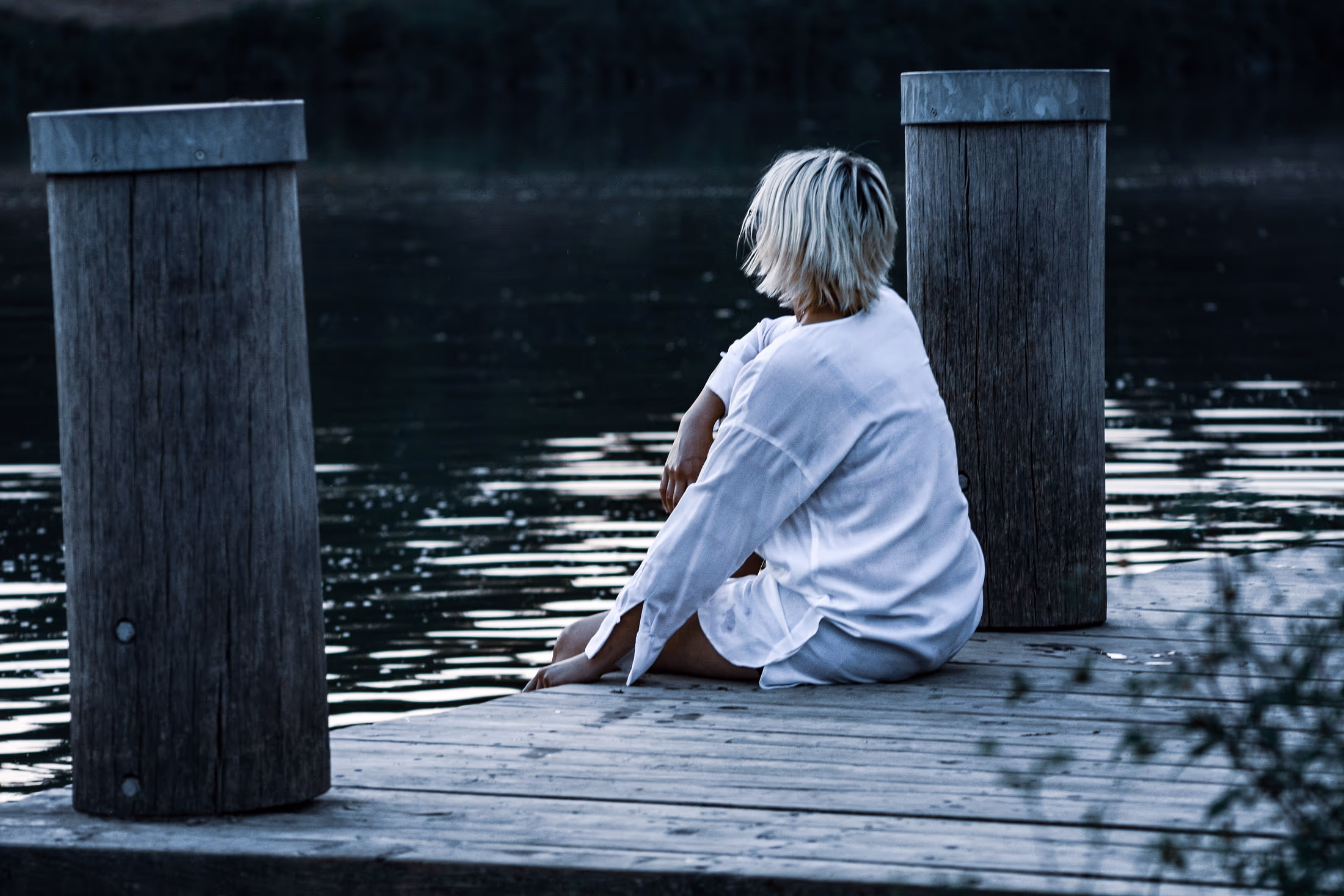 Kind sitzt allein auf einem Holzsteg am Wasser