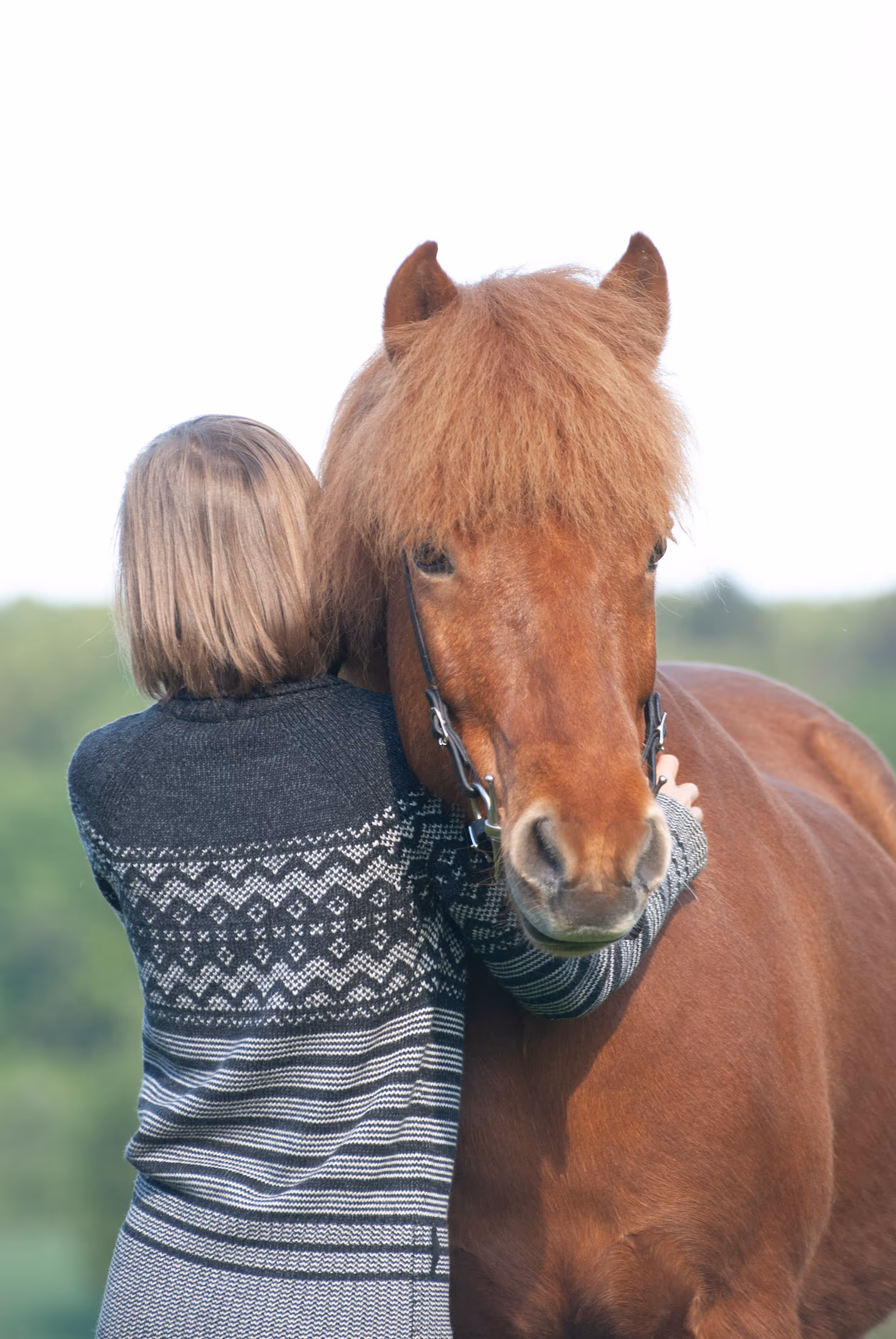 Blonder Kopf an den Hals eines Pferdes gelehnt, die Arme um seinen Kopf